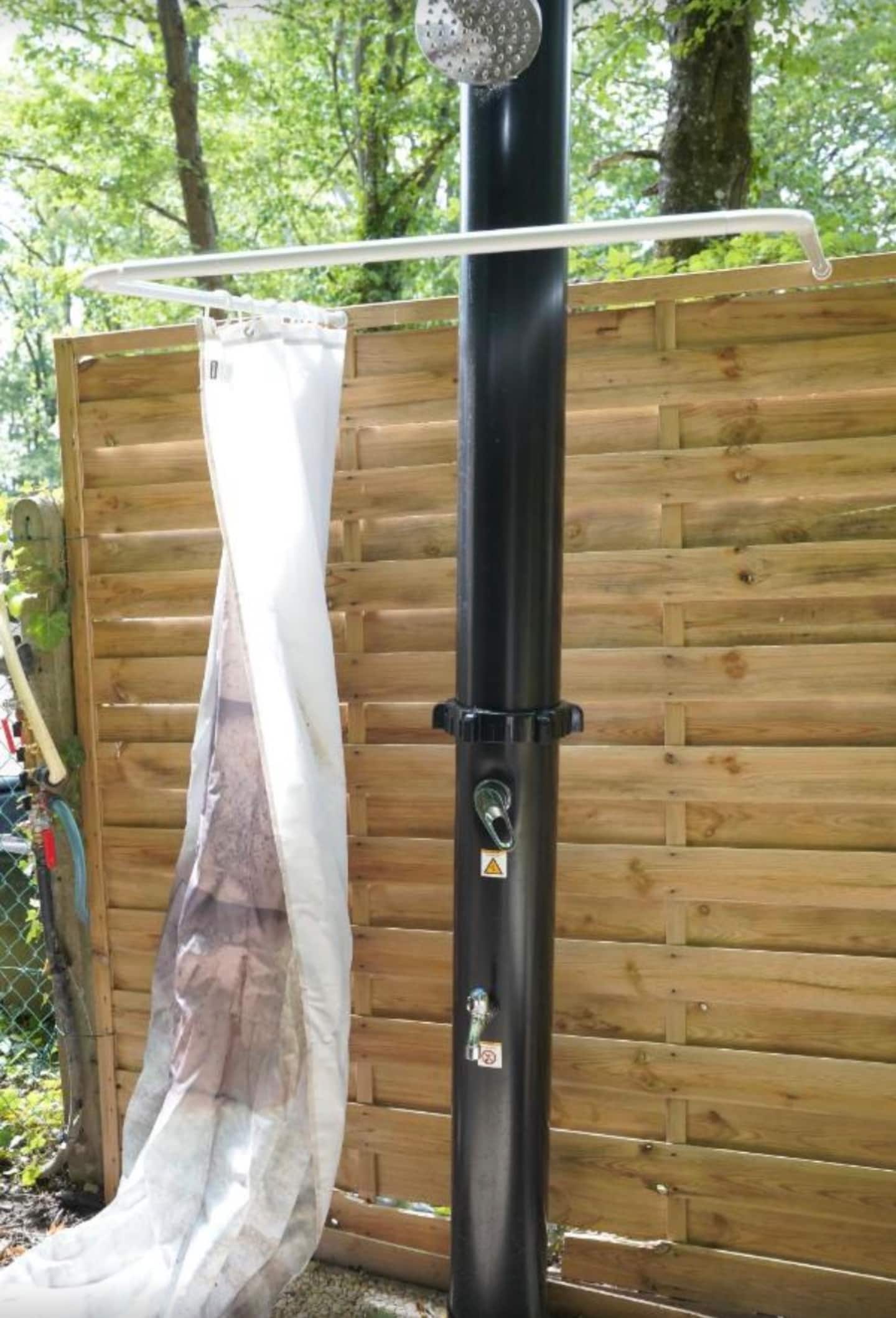 La douche solaire extérieure, adossée à une palissade en bois