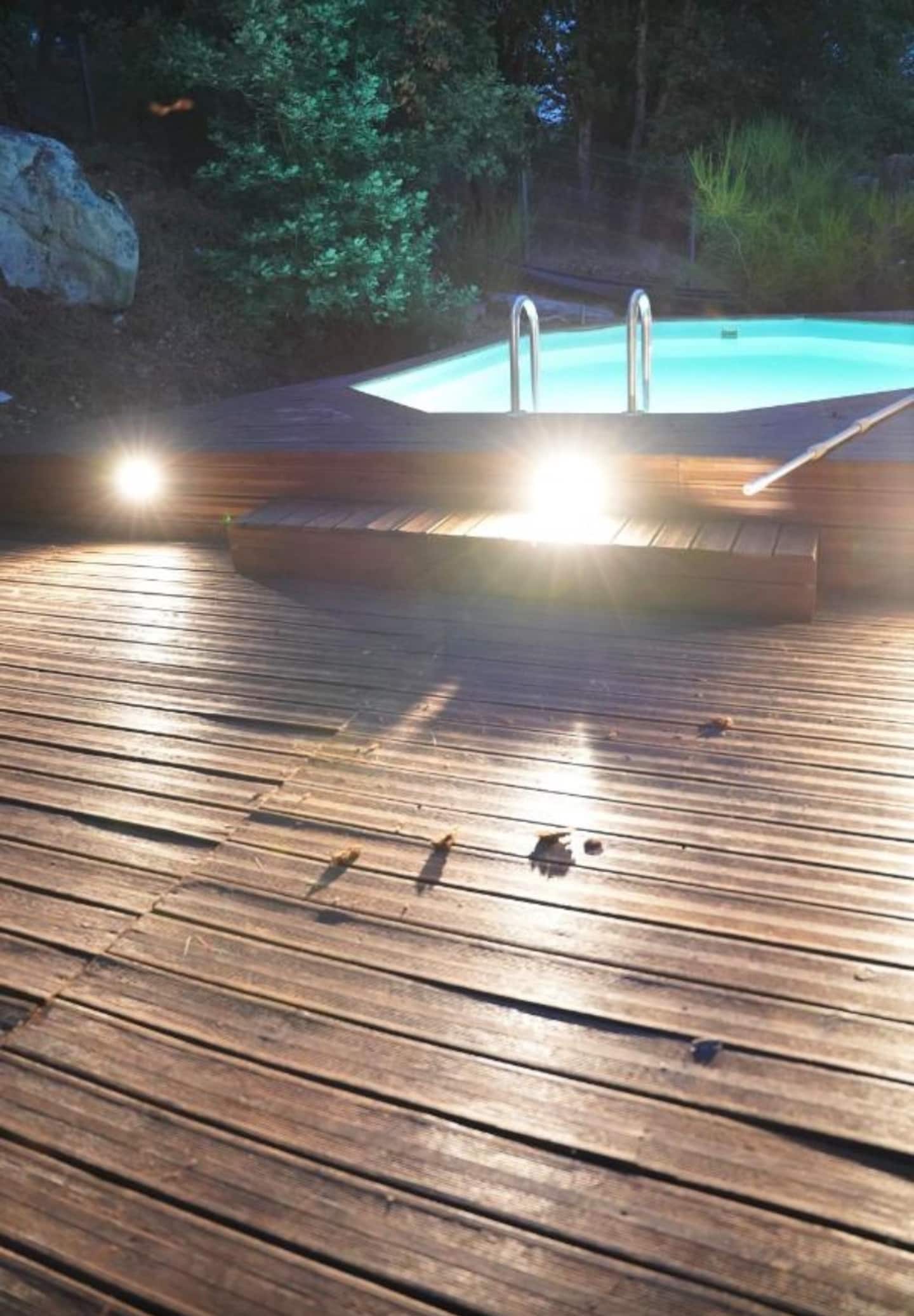 La terrasse en bois et la piscine éclairées à la tombée de la nuit